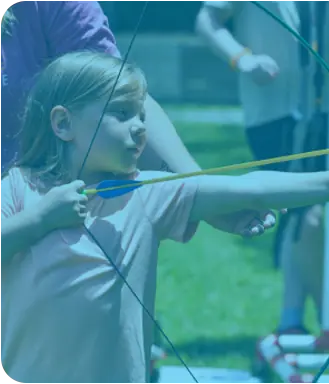 A child drawing a bow at archery, guided by a Y instructor.