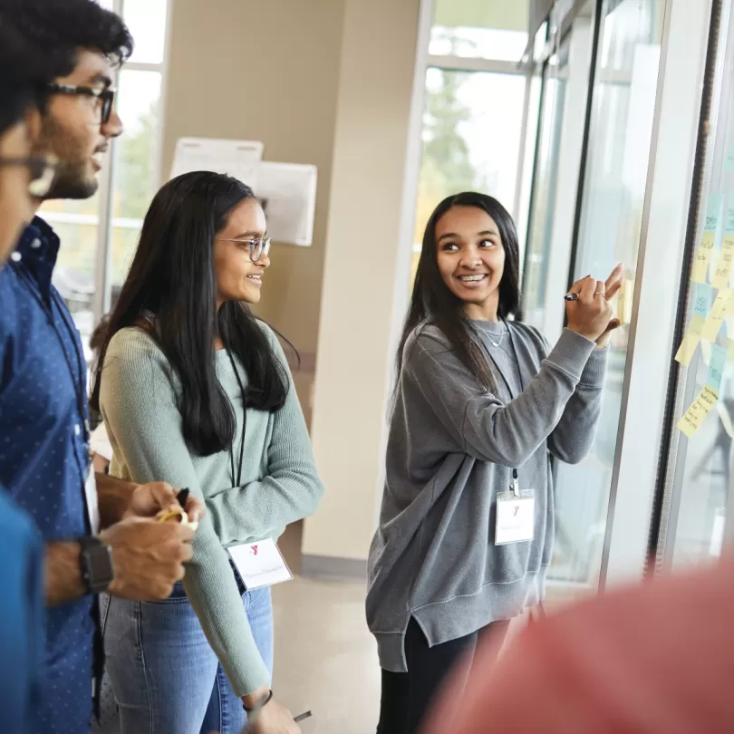 teen writing on dry-erase board smiling back at several peers in her group
