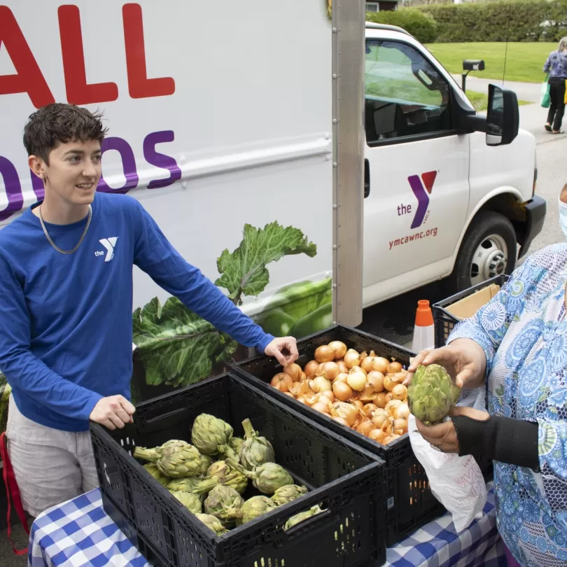 Y Staff standing near baskets of fresh fruits and vegetables while communities members walk through picking out their fresh produce