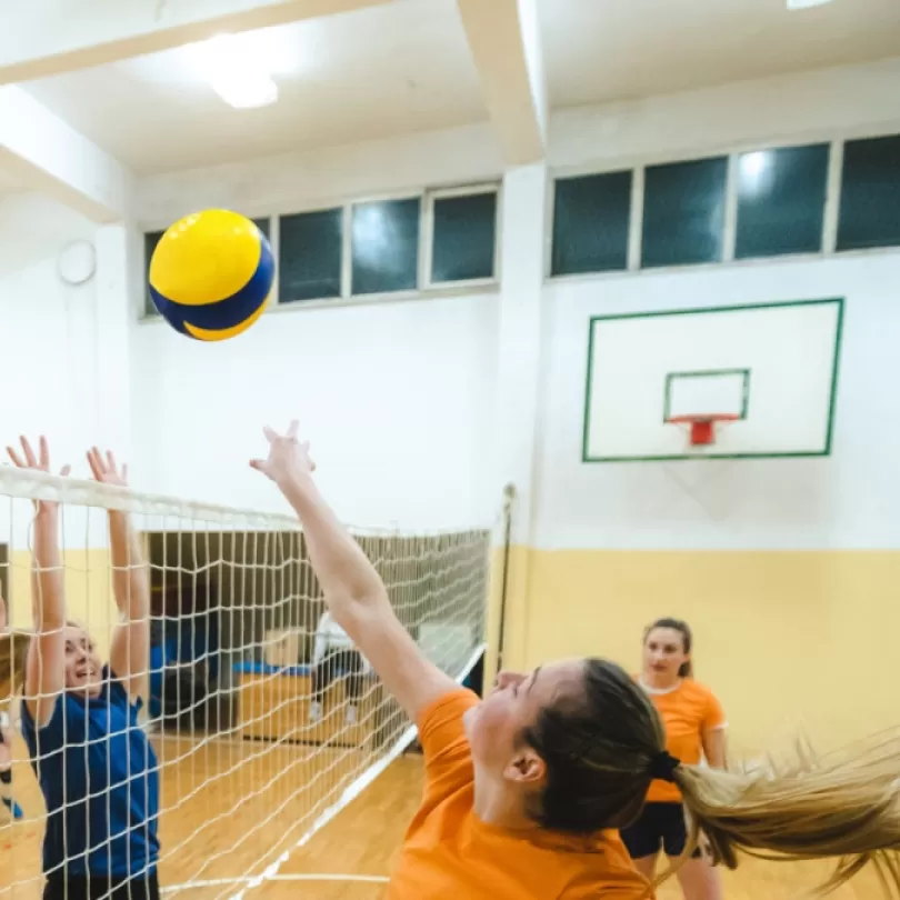 Group of adults play volleyball in a gym.