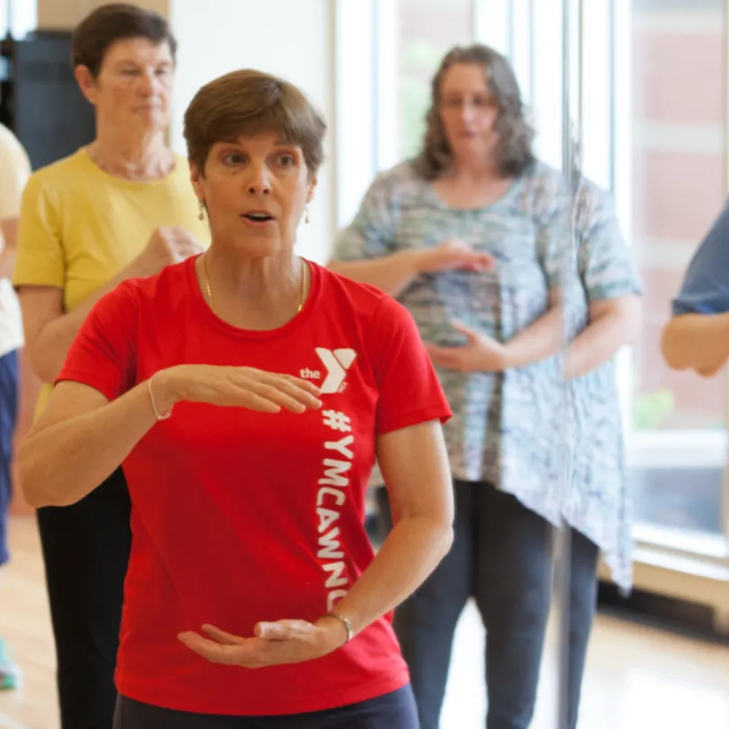 A woman teaches a group exercise class of older adults.