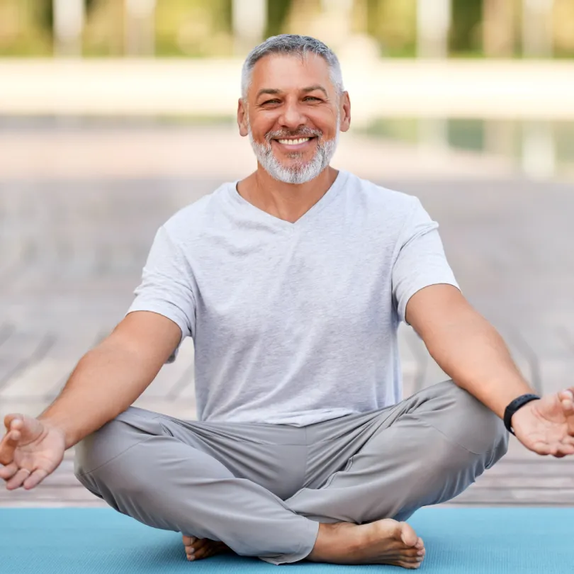 A man smiles as he does yoga outside.