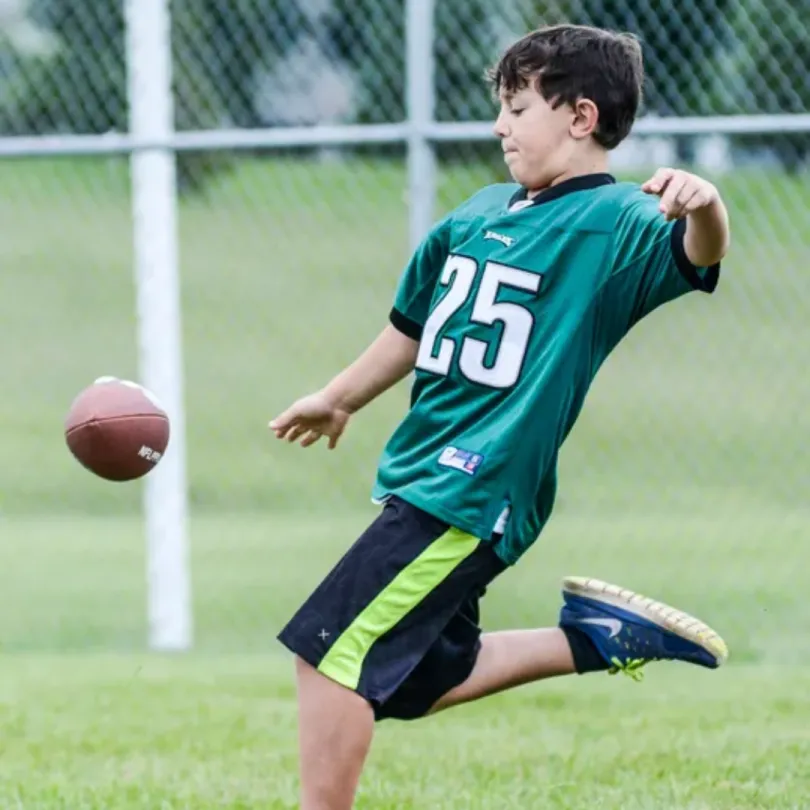 A kid kicking a football on an outdoor field.
