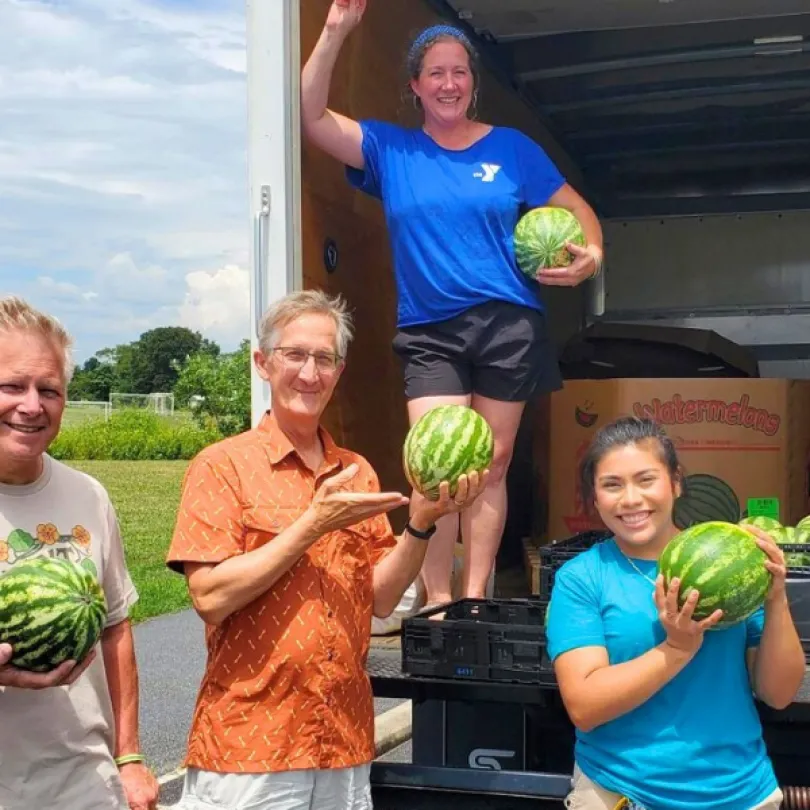 A group of volunteers hold watermelons at a YMCA Mobile Food Market.