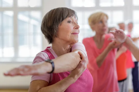 Two active aging women stretch in group exercise class