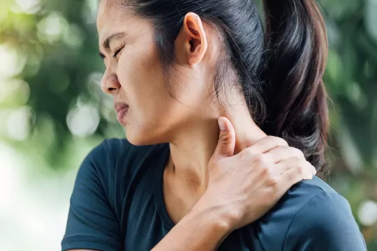 A woman with neck pain rubs her shoulder.