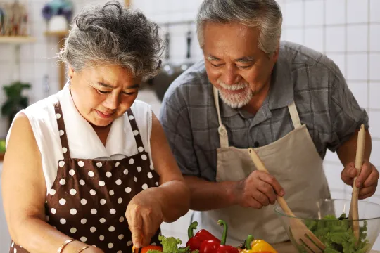 An older adult couple prepare a healthy salad in the kitchen.
