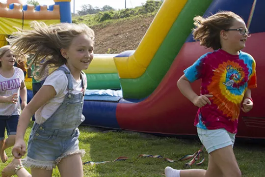 Two kids smile as they run outside at a fair.