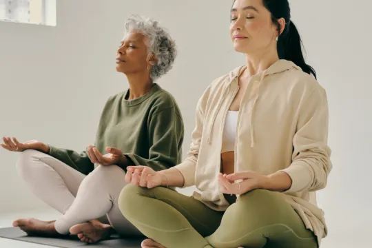 Two women sit on the floor in a yoga pose during a class.