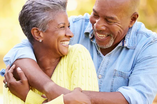 An older couple embrace and smile at each other as they sit outside.