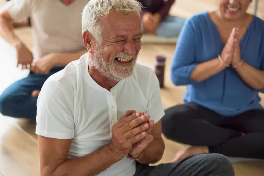 A man laughs while doing yoga in a group class.
