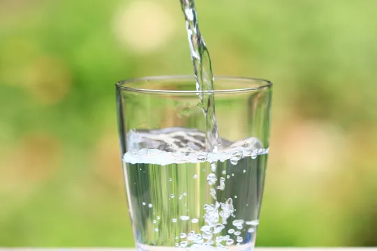 A glass sitting on a table outside being filled with water.