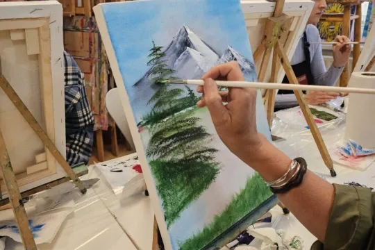 A close-up of someone painting in a Bob Ross painting class.
