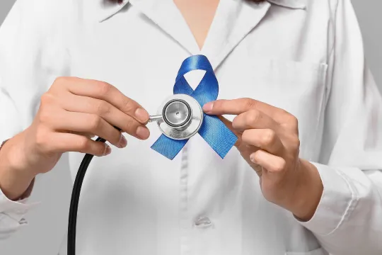 A doctor holding a blue cancer ribbon and a stethoscope.