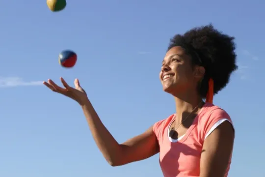 A woman smiles as she learns how to juggle.