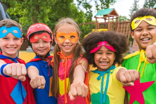 A group of kids dressed as superheroes smile and play outside.