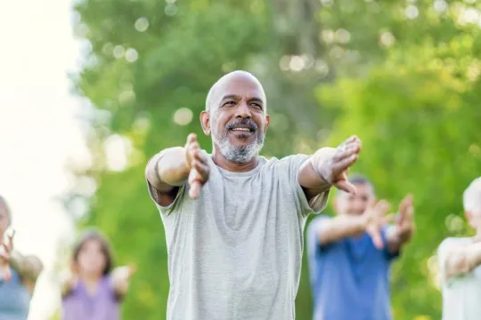 A group of older adults participate in a tai chi group exercise class outside.