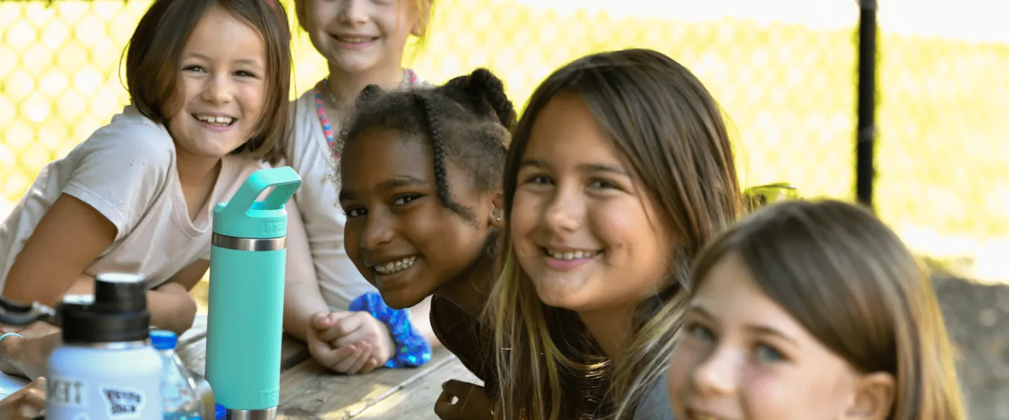 A group of five elementary age girls smile at the camera as they sit outside in an afterschool program.