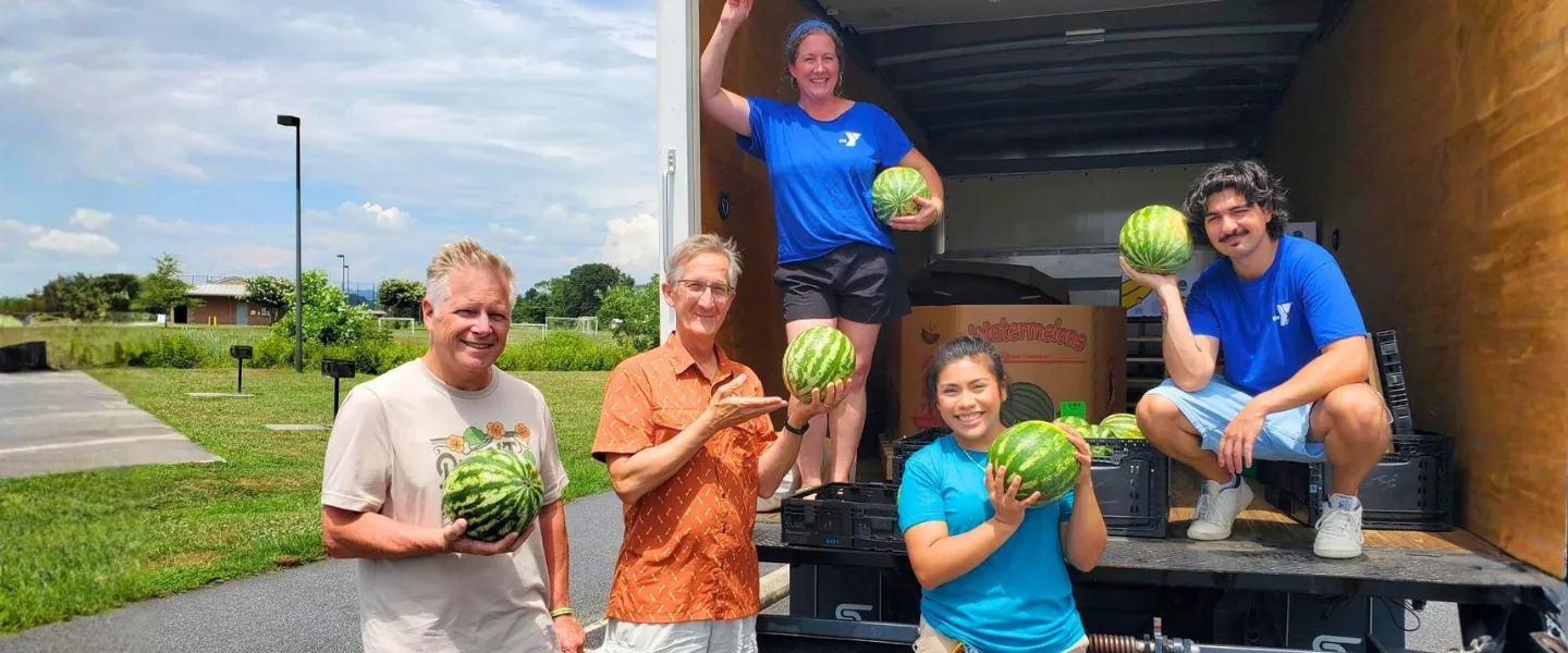 A group of volunteers hold watermelons at a YMCA Mobile Food Market.