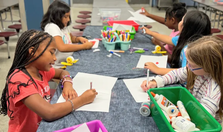 A group of girls at YMCA summer camp color at a table.