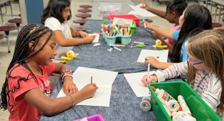 A group of girls at YMCA summer camp color at a table.