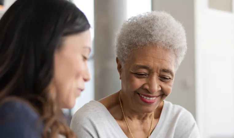 An elderly patient smiling and sitting next to her doctor as they discuss medical information.
