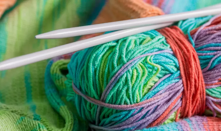 A close-up of two knitting needles and a skein of yarn. The yarn is brightly multicolored.