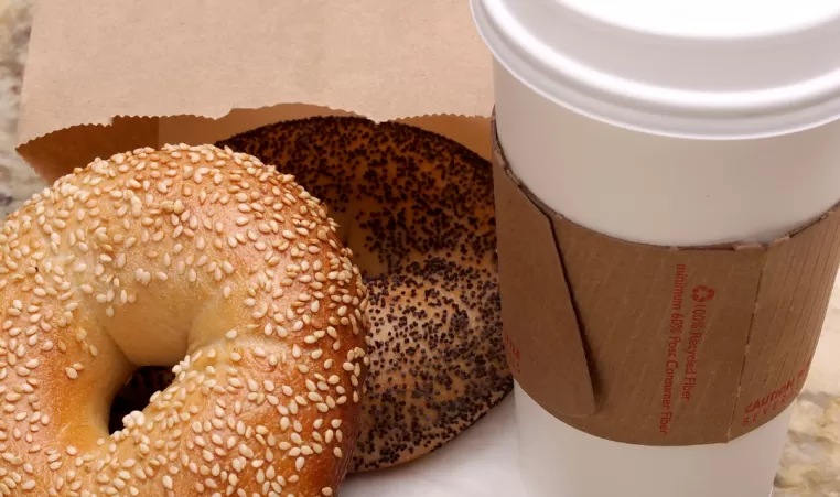 Two bagels lie on top of a napkin. A paper cup of coffee sits next to them on a countertop.