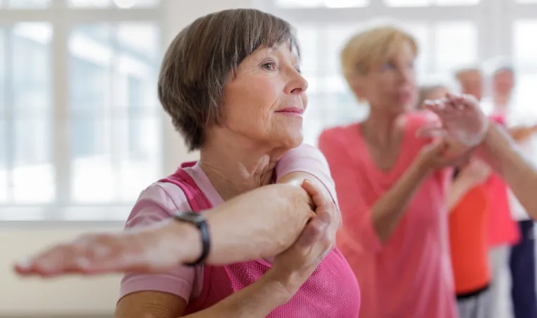 Two active aging women stretch in group exercise class