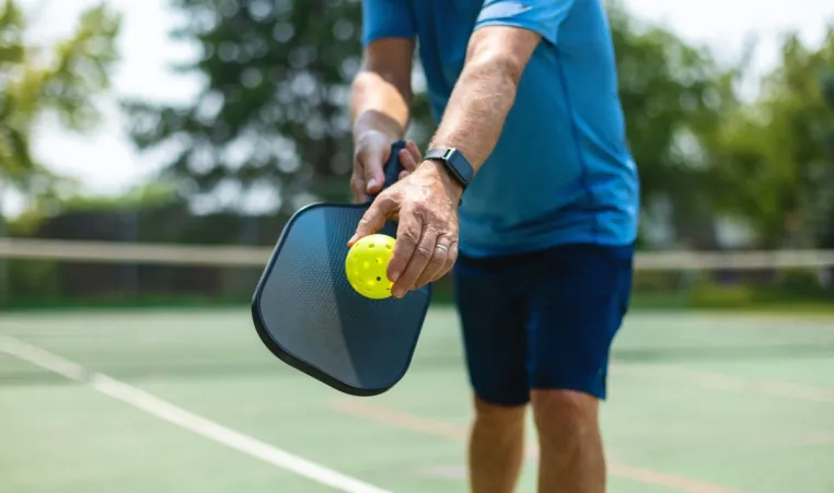 A closeup of a man playing pickleball outside.