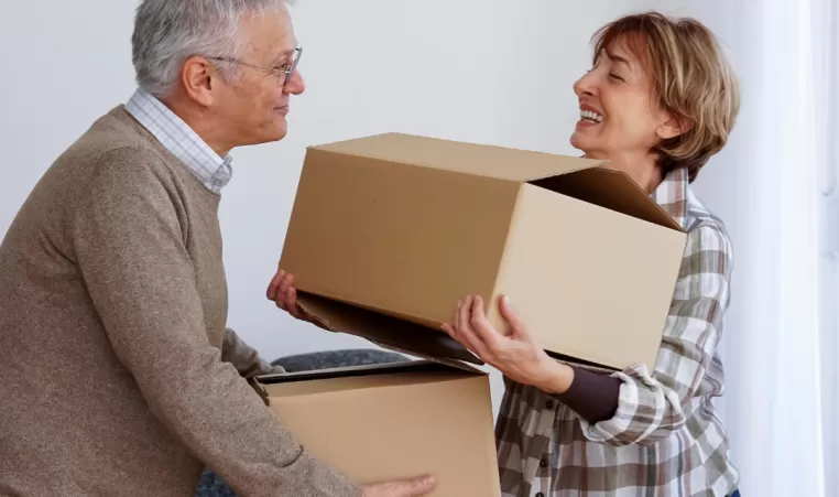 An older couple is stacking boxes on top of each other and carrying them.