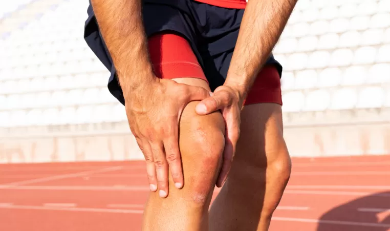 A runner on a track reaches down to hold their knee in pain.