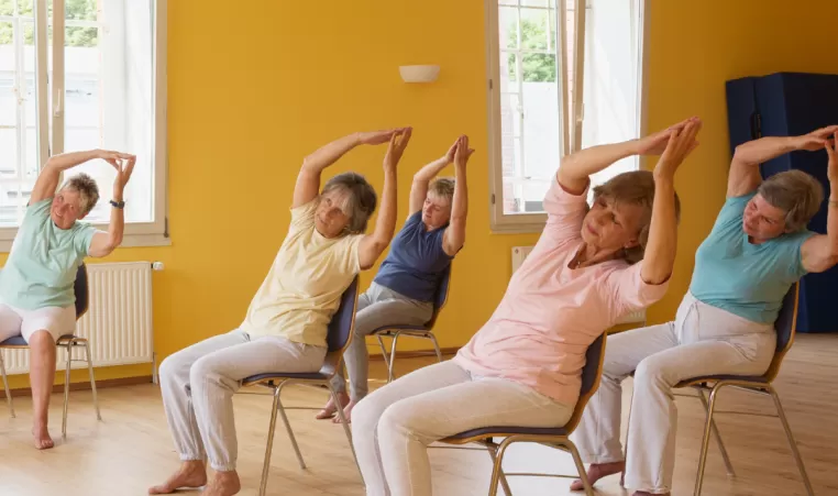 A group of older women participate in a chair yoga class.