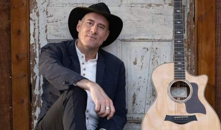 A picture of David LaMotte. He is sitting on the ground next to his guitar.