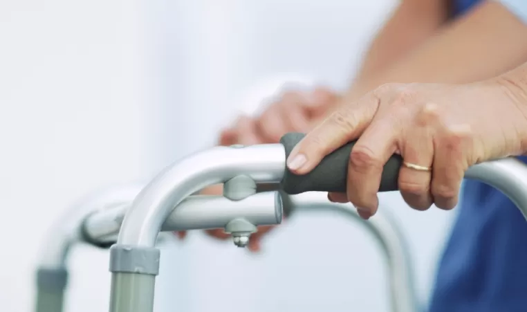 A pair of hands hold onto a walker as they walk.