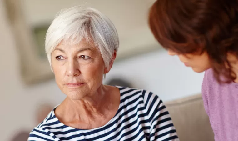 An older woman looks out the window and holds hands with her daughter.