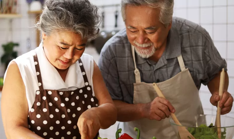 An older adult couple prepare a healthy salad in the kitchen.