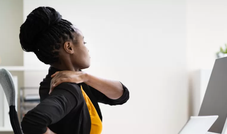 A woman stretches her shoulder while sitting at her work desk.