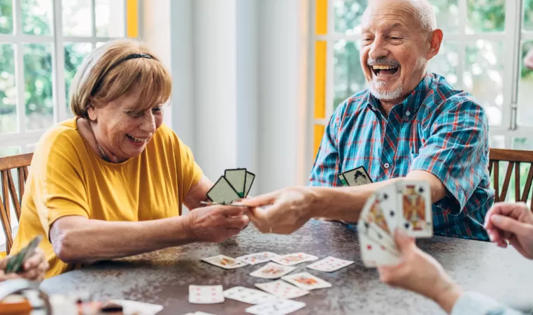 A group of older adults laugh and play a card game together.