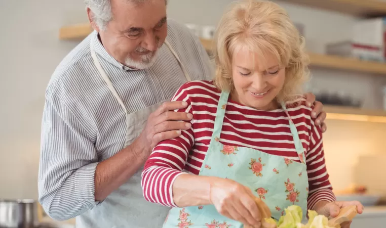 An older couple make a salad in the kitchen.