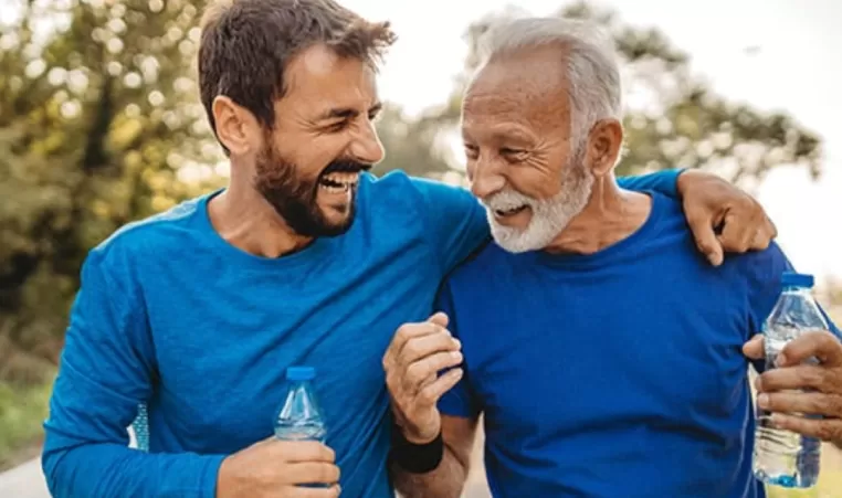 A father and son laugh as they drink water and exercise outdoors.