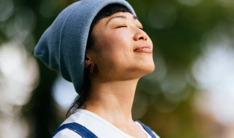 A woman stands outside with her eyes closed. She has a content expression on her face.