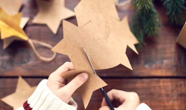 A closeup of a pair of hands cutting holiday shapes out of paper.