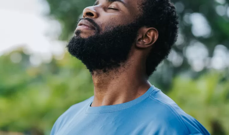 A man stands outside with his eyes closed. He has a relaxed look on his face.