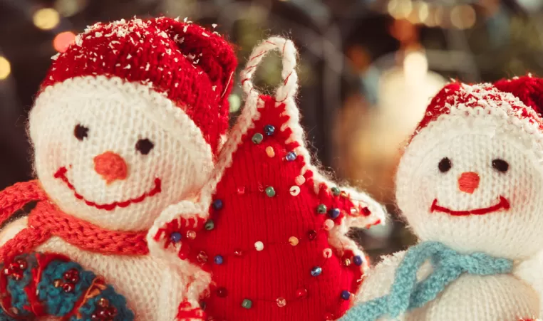 A close up picture of handmade holiday crafts. There are two stuffed snowmen and a red stuffed Christmas tree.
