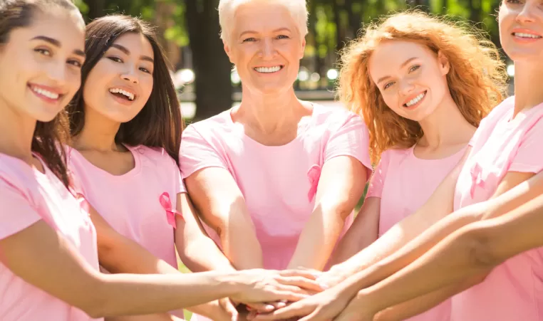 A group of women smile as they put their hands together in support of a healthy lifestyle.