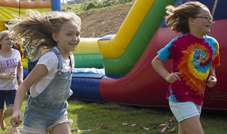 Two kids smile as they run outside at a fair.