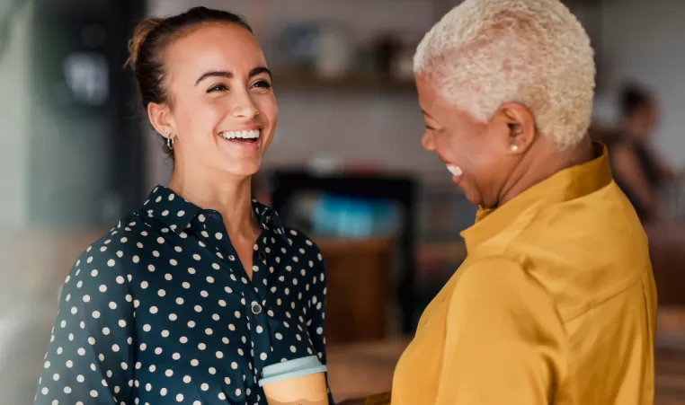 Two women smile as they have a conversation while getting coffee together.
