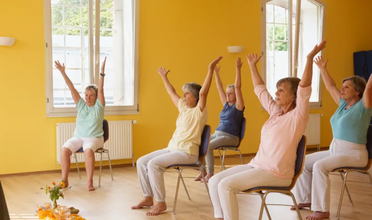 A group of women participate in a modified chair exercise class.
