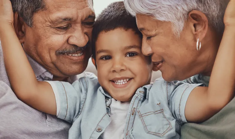 A boy smiles and hugs both of his grandparents.